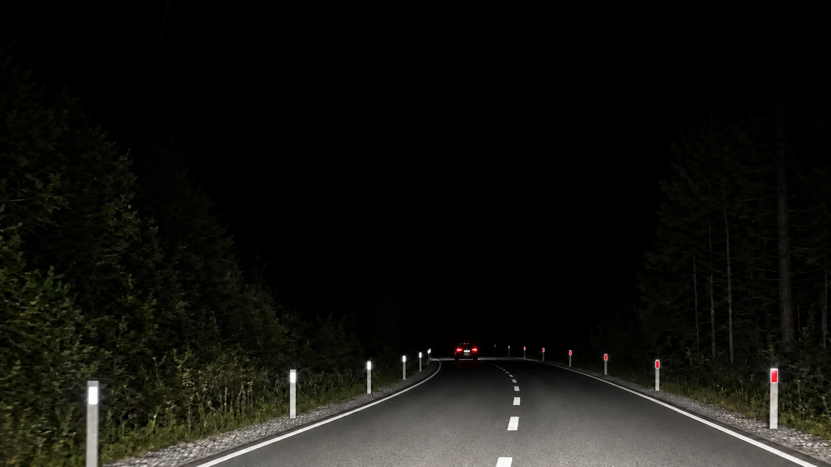 Night road lined with GRP roadside flexible delineator posts: red reflectors on the driver's right, white on the left, a warning sign ahead of the bend